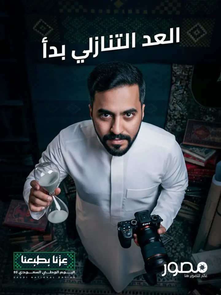 Seasonal post for a photographer booking platform: a man in a thobe holding an hourglass and a camera in a majlis